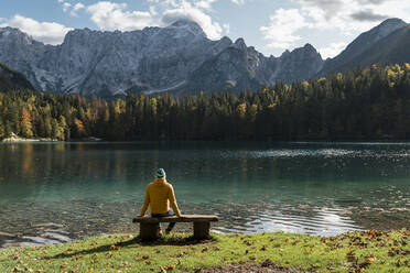 Hiker sitting on bench at Laghi di Fusine, Friuli Venezia Giulia, Italy - MAUF03229