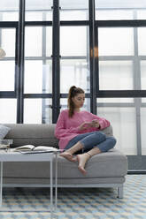Young woman sitting barefoot on the couch using cell phone - ERRF02571