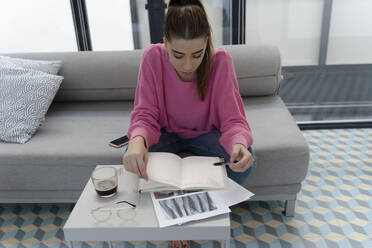 Young woman sitting on the couch looking at order book - ERRF02574