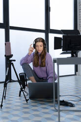 Porträt einer jungen Frau, die mit Laptop und Smartphone in einem Studio Aufnahmen macht - ERRF02593