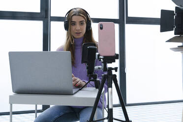 Porträt einer jungen Frau, die mit Laptop und Smartphone in einem Studio Aufnahmen macht - ERRF02597