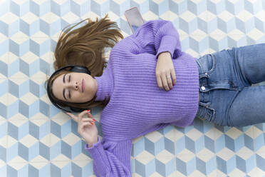 Porträt einer jungen Frau mit geschlossenen Augen, die auf dem Boden liegt und mit Kopfhörern Musik hört - ERRF02598