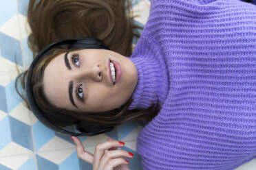 Porträt einer jungen Frau, die auf dem Boden liegt und mit Kopfhörern Musik hört - ERRF02599