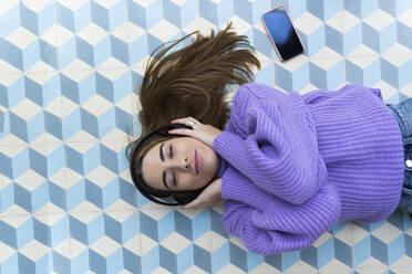 Portrait of young woman with eyes closed lying on the floor listening music with headphones - ERRF02600