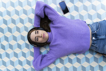 Portrait of happy young woman lying on the floor listening music with headphones - ERRF02601