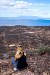 Rückansicht einer Frau, die auf einem Aussichtspunkt sitzt, Teneriffa, Spanien - SIPF02118