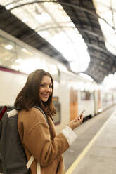 Portrait of smiling young woman with cell phone at the train station - VABF02493