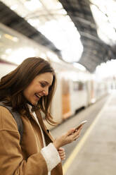 Glückliche junge Frau mit Handy am Bahnhof - VABF02495