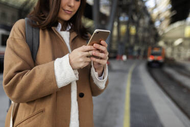 Nahaufnahme einer Frau, die am Bahnhof ein Mobiltelefon benutzt - VABF02502