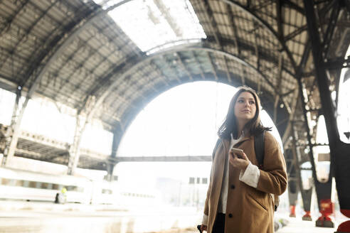 Junge Frau mit Mobiltelefon am Bahnhof, die sich umschaut - VABF02503