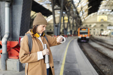 Junge Frau prüft die Uhrzeit am Bahnhof - VABF02504