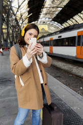 Junge Frau mit Kopfhörern und Mobiltelefon am Bahnhof - VABF02509