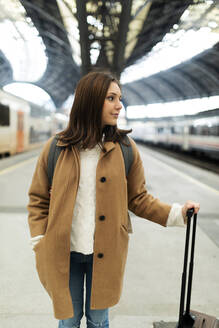 Junge Frau mit Koffer auf dem Bahnhof, die sich umschaut - VABF02515