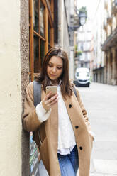 Junge Frau überprüft ihr Telefon in der Stadt, Barcelona, Spanien - VABF02538