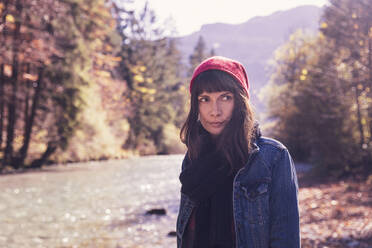 Woman wearing red woolly hat and denim jacket at riverside - DHEF00014