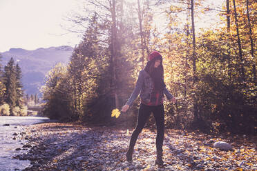 Woman wearing red woolly hat and denim jacket walking at riverside in autumn - DHEF00015