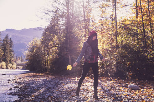 Woman wearing red woolly hat and denim jacket walking at riverside in autumn - DHEF00015