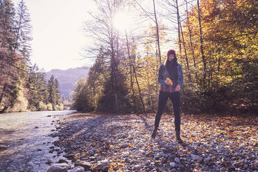 Woman wearing red woolly hat and denim jacket walking at riverside in autumn - DHEF00016