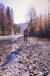 Woman wearing red woolly hat and denim jacket walking at riverside in autumn - DHEF00019