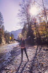 Woman with raised arms at riverside in autumn - DHEF00025