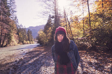 Woman wearing red woolly hat and denim jacket at riverside in autumn - DHEF00026