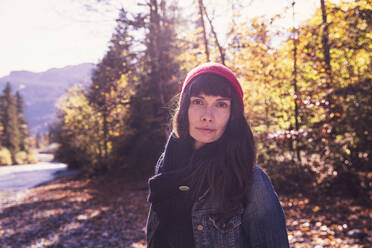 Woman wearing red woolly hat and denim jacket at riverside in autumn - DHEF00027