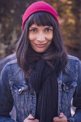 Portrait of smiling woman wearing red woolly hat and denim jacket - DHEF00029