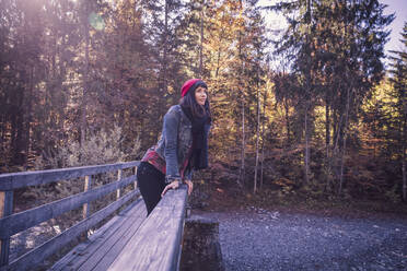 Woman wearing red woolly hat and denim jacket on a bridge in autumn - DHEF00032