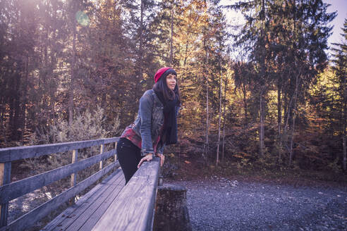 Frau mit roter Wollmütze und Jeansjacke auf einer Brücke im Herbst - DHEF00032