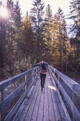 Woman wearing red woolly hat and denim jacket running on a bridge in autumn - DHEF00034
