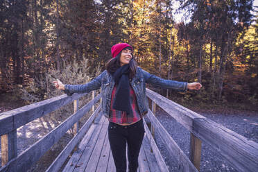 Woman wearing red woolly hat and denim jacket on a bridge in autumn - DHEF00035