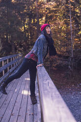 Woman wearing red woolly hat and denim jacket on a bridge in autumn - DHEF00036