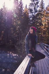 Woman wearing red woolly hat and denim jacket sitting on a railing and looking sideways - DHEF00038