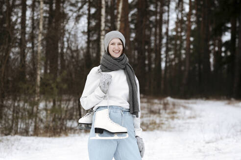 Porträt einer glücklichen Frau mit Schlittschuhen im Winter - EYAF00811