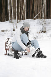 Frau zieht Schlittschuhe auf einem Schneefeld an - EYAF00812