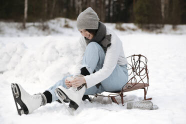 Lächelnde Frau beim Anziehen von Schlittschuhen auf einem Schneefeld - EYAF00815