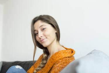 Porträt einer lächelnden jungen Frau mit Zopf auf einer Couch sitzend - JPTF00430