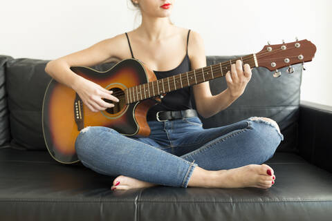 Crop-Ansicht einer jungen Frau, die auf einer Couch sitzt und Gitarre spielt, lizenzfreies Stockfoto