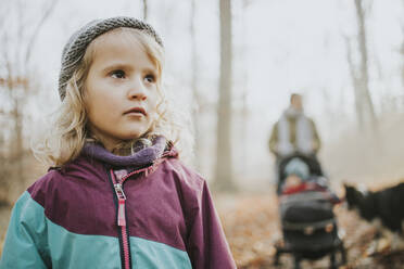 Blond girl with her mother, sister and border collie in the background during forest walk in autumn - DWF00550