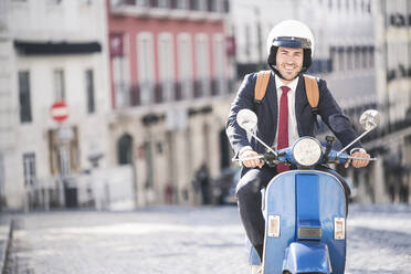 Porträt eines lächelnden jungen Geschäftsmannes auf einem Motorroller in der Stadt, Lissabon, Portugal - UUF20067