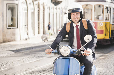 Junger Geschäftsmann auf einem Motorroller in der Stadt, Lissabon, Portugal - UUF20069
