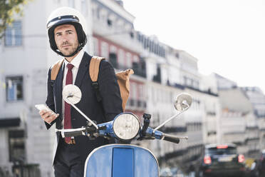 Young businessman with cell phone and motor scooter in the city, Lisbon, Portugal - UUF20075