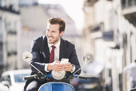 Young businessman with cell phone on motor scooter in the city, Lisbon, Portugal stock photo