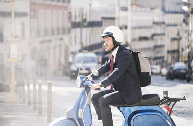 Young businessman riding motor scooter in the city, Lisbon, Portugal - UUF20088