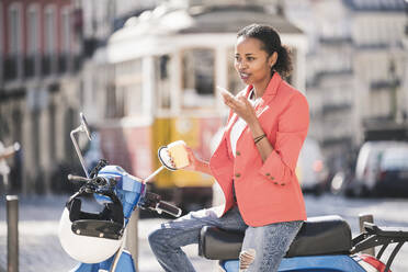 Young woman with motor scooter using cell phone in the city, Lisbon, Portugal - UUF20094