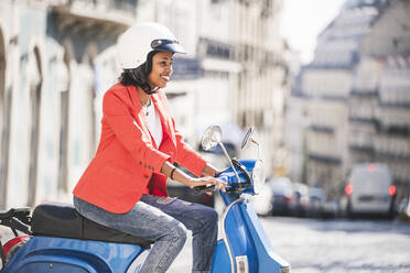 Lächelnde junge Frau auf einem Motorroller in der Stadt, Lissabon, Portugal - UUF20100