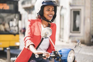Lächelnde junge Frau auf einem Motorroller in der Stadt, Lissabon, Portugal - UUF20103