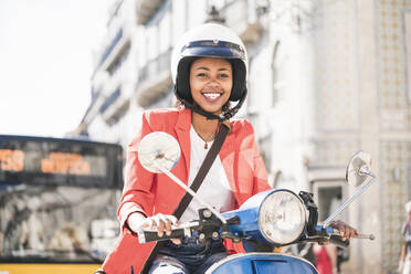 Portrait of happy young woman riding motor scooter in the city, Lisbon, Portugal - UUF20105