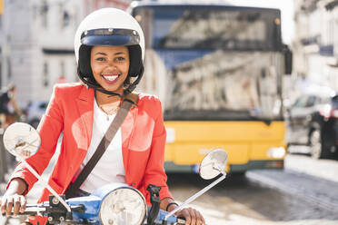 Portrait of happy young woman riding motor scooter in the city, Lisbon, Portugal - UUF20106