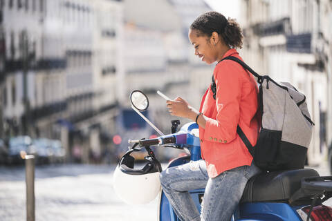 Junge Frau benutzt Handy auf Motorroller in der Stadt, Lissabon, Portugal, lizenzfreies Stockfoto